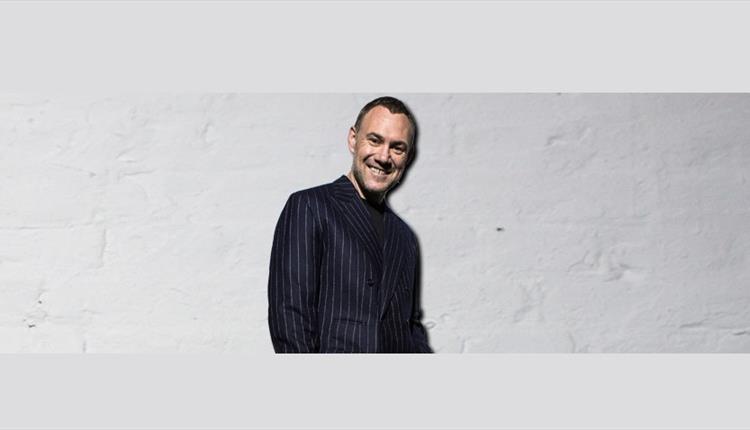 David Gray smiling on a white brick background