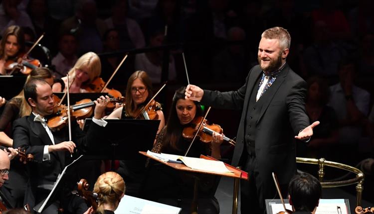 Composer smiling in a suit with group of people and instruments in a spotlight