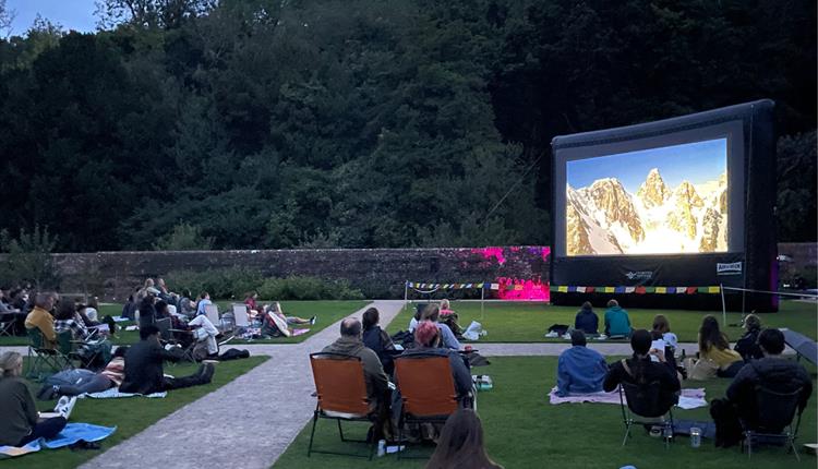 people spaced out on blankets and chairs in an outdoor garden watching a movie