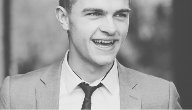 A cropped black and white image of a man with a suit and tie on.