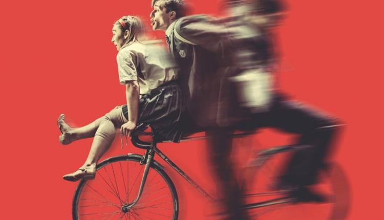 Three people on one bike against a red background